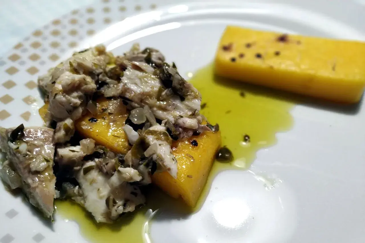 Piatto di luccio in umido con polenta gialla, condito con erbe aromatiche e olio. Un sapore autentico da provare!