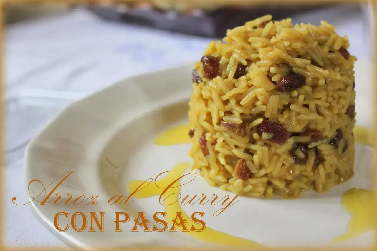 Arroz al curry con pasas, un plato aromático y dulce servido en un plato blanco con un toque de salsa dorada.