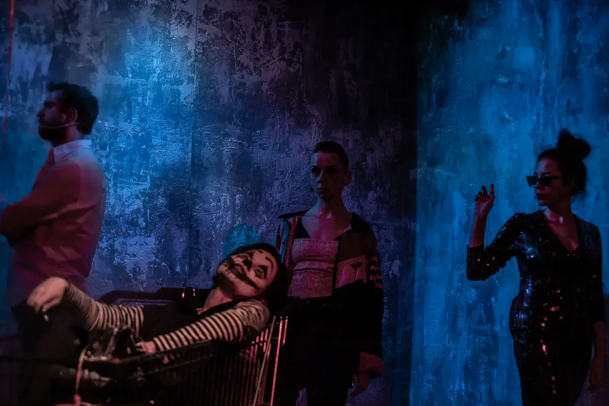 Scena z teatru Barakah. Aktor w wózku, klaun z makijażem, kobieta w cekinowej sukience i mężczyzna w białej koszuli.