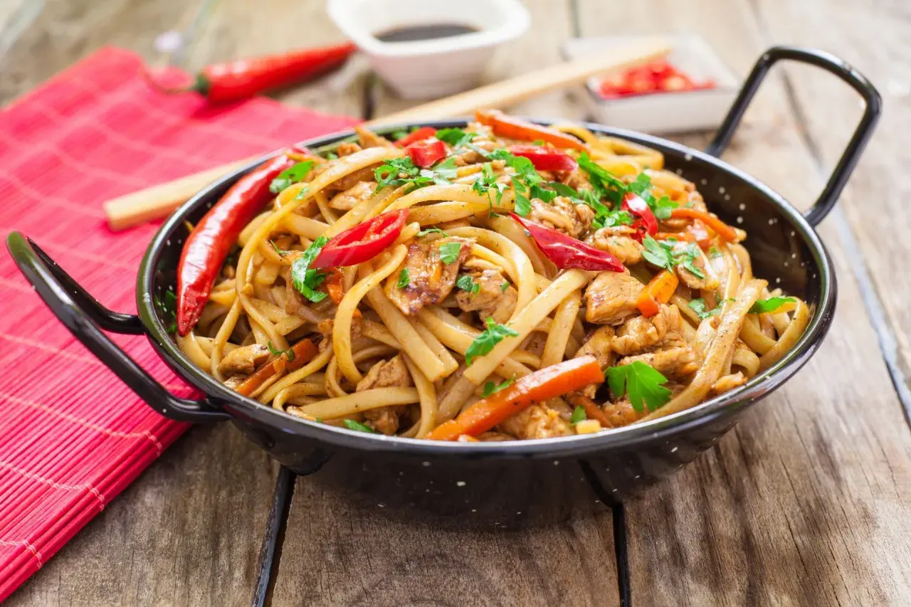 Pyszny makaron chow mein z kurczakiem, papryką i chili, posypany świeżą pietruszką.