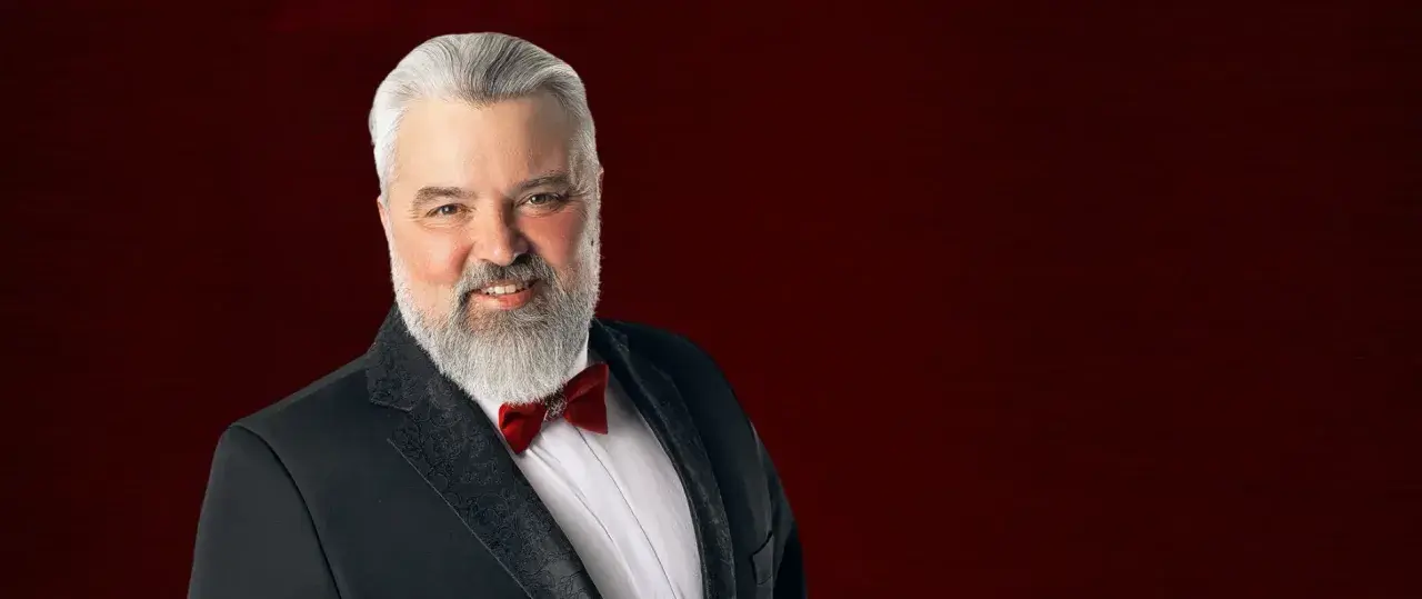 Mirosław Niewiadomski, tenor, w czarnym smokingu z czerwoną muszką, uśmiecha się do widza.