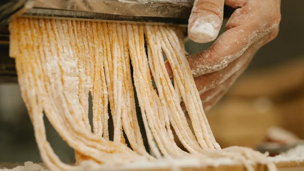 Färska pastastrådar skärs från en pastamaskin, en påminnelse om vart kommer pasta ifrån.