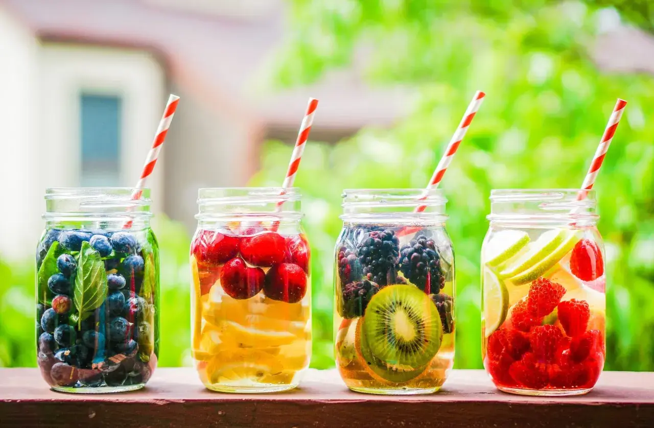 Quattro barattoli con acqua detox: mirtilli, ciliegie e limone, more e kiwi, lamponi e lime.