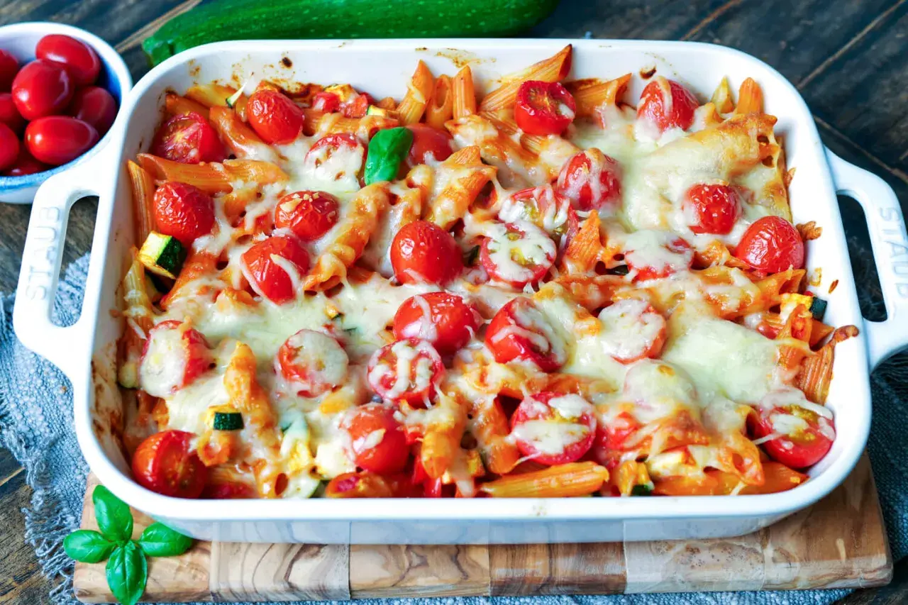 Ein köstlicher nudelauflauf vegetarisch mit Penne, Kirschtomaten und geschmolzenem Käse, garniert mit frischem Basilikum.