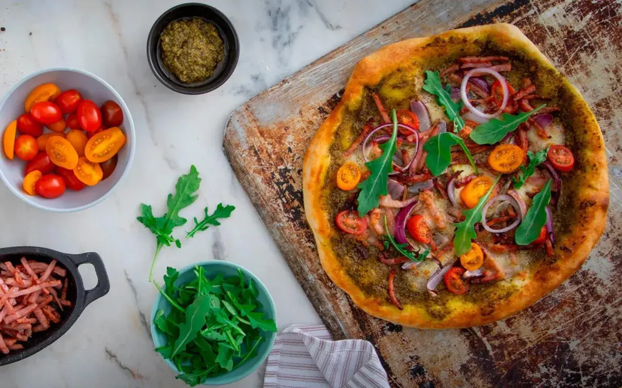 En läcker pizza bianco med parmaskinka, ruccola, körsbärstomater och rödlök. Perfekt för en mysig kväll!