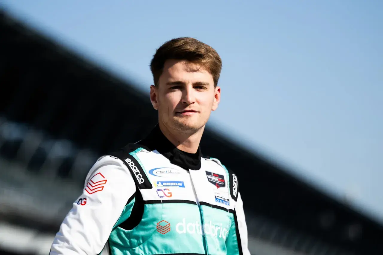 Logan Sargeant, piloto de carreras, posa con su traje de competición blanco y turquesa, listo para la acción.