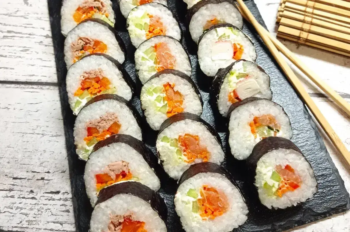 Pyszne domowe sushi z łososiem, tuńczykiem i warzywami, ułożone na czarnej desce.