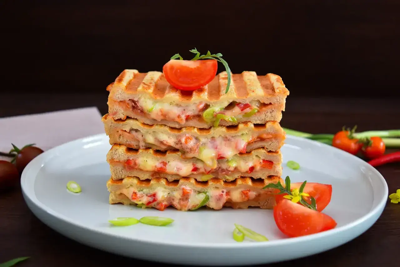 Gestapelte Sandwiches mit geschmolzenem Käse und Gemüse, perfekt für kontaktgrill rezepte. Garniert mit Tomaten und Frühlingszwiebeln.