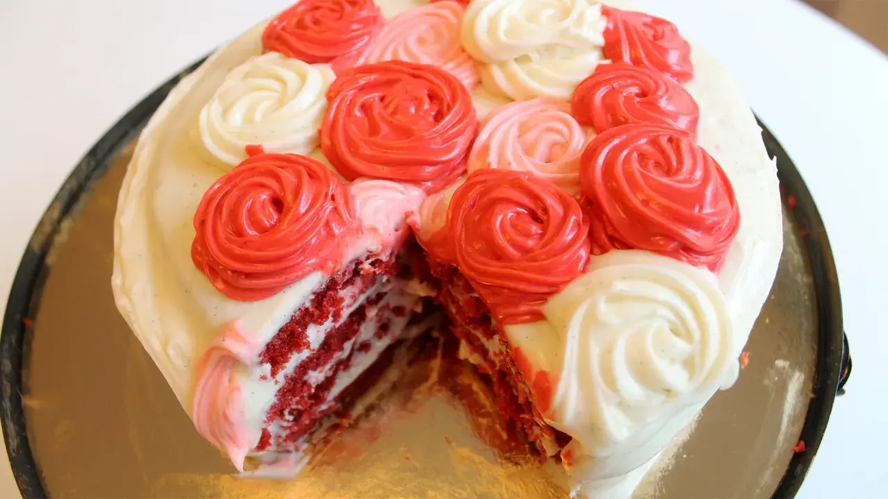 En skivad red velvet cake med vit frosting och dekorationer i form av röda och rosa rosor.