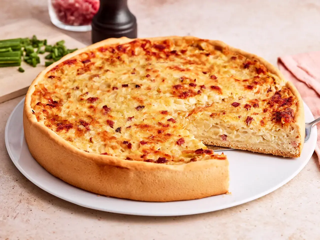 Ein goldbrauner Zwiebelkuchen mit Speck, bereit zum Servieren. Ein Stück fehlt, was Lust auf mehr macht. Perfekt für ein Zwiebelkuchen Rezept.