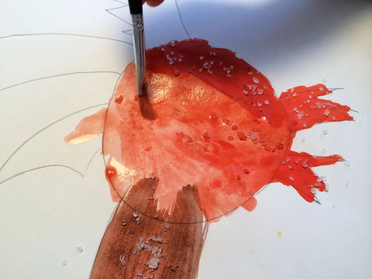 Ein Pinsel trägt rote Farbe auf, während grobes Salz auf dem nassen Aquarellpapier liegt. Diese Salz-Bilder entstehen durch die Reaktion von Salz und Farbe.