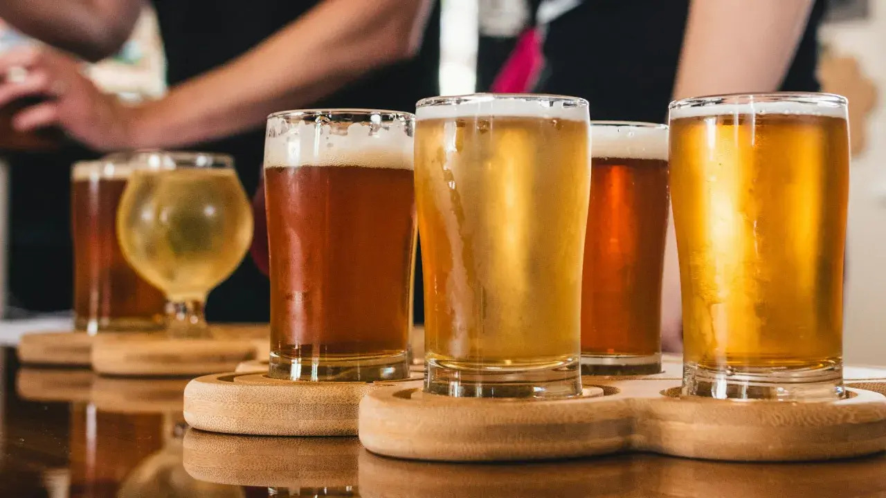 Assaggio di birra danese: bicchieri di diverse birre ambrate e dorate, con schiuma cremosa, su un vassoio di legno.