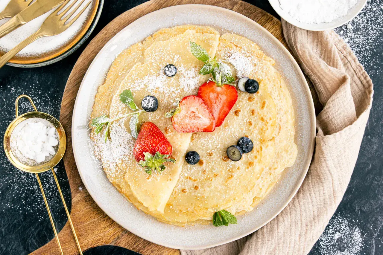 Dünne Pfannkuchen mit Hafermilch, bestäubt mit Puderzucker und garniert mit frischen Erdbeeren und Blaubeeren.