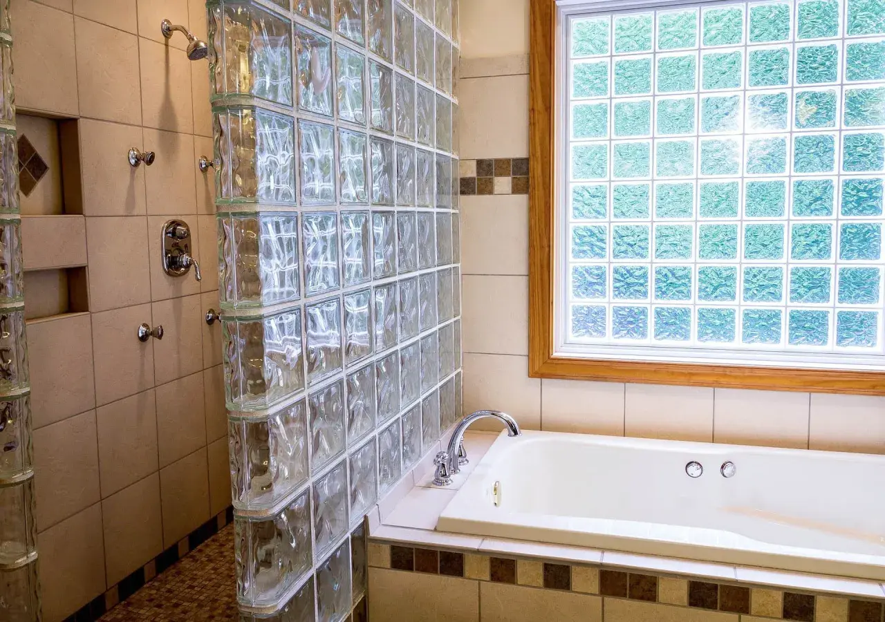 Duchas con paves de vidrio separan la bañera de la zona de ducha. La luz se filtra a través de la ventana de paves.