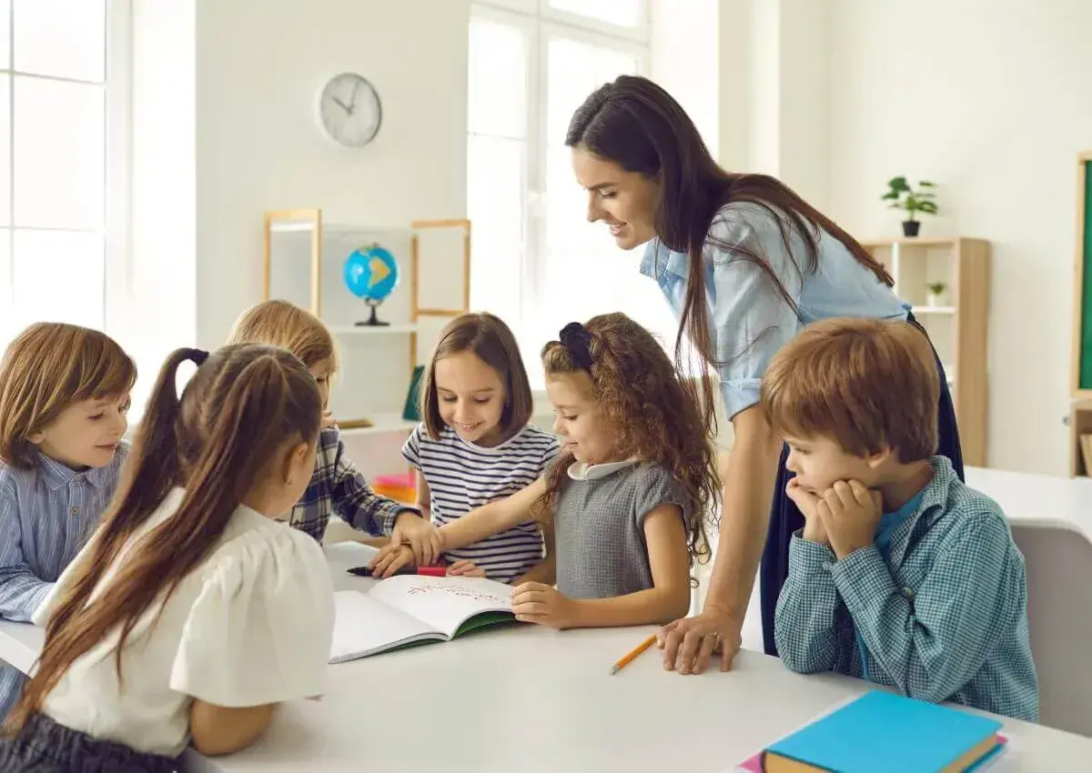 Lehrerin unterstützt Kinder bei ihrer Projektarbeit. Sie arbeiten gemeinsam an einem Buch, lernen und lachen.
