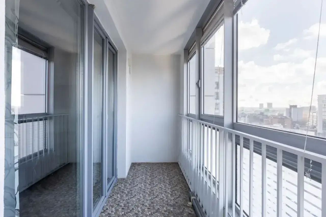 Nowoczesna zabudowa balkonu w bloku z dużymi oknami i widokiem na miasto.