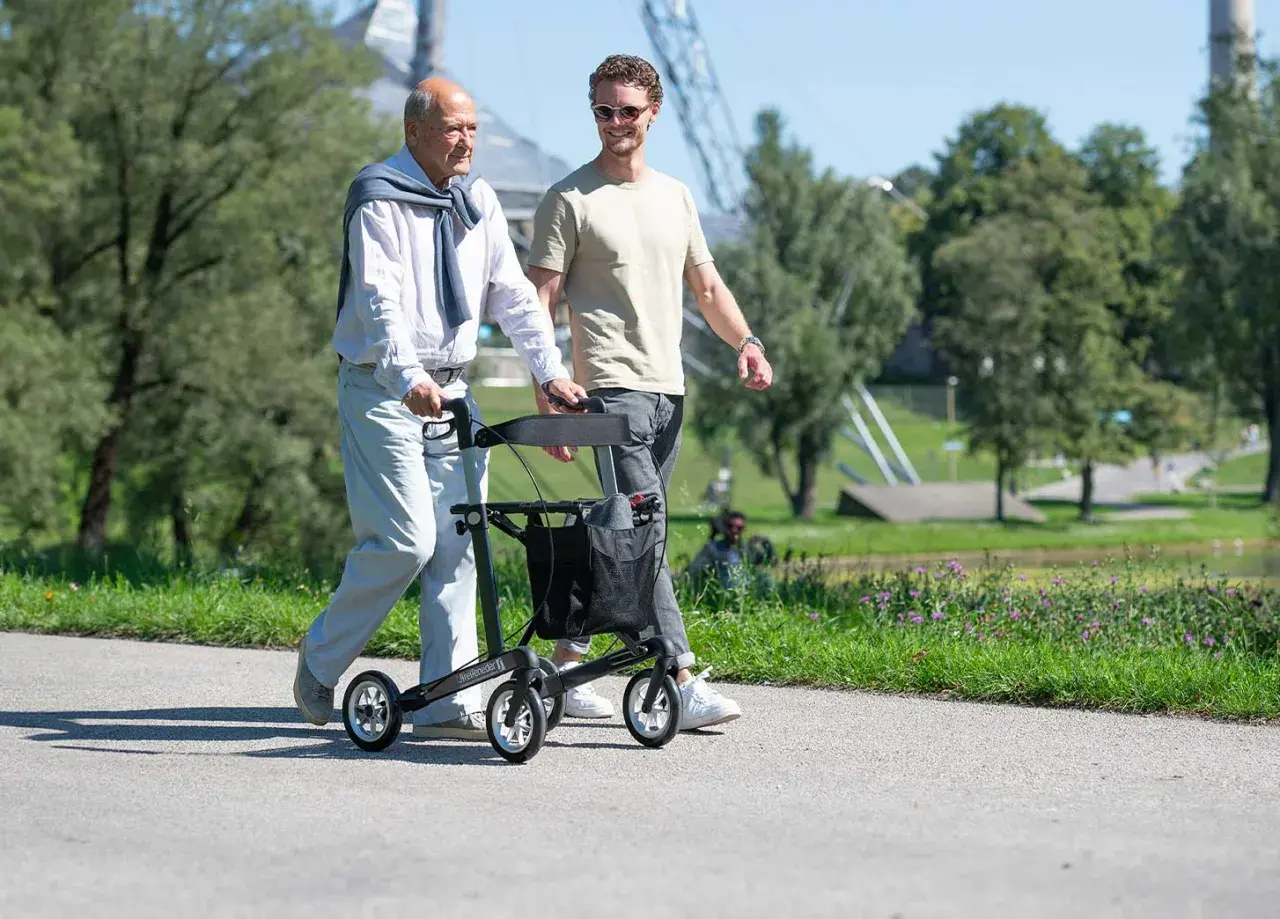 Ein älterer Mann geht mit einem Rollator spazieren, der ihm Halt gibt. Es gibt verschiedene Gehhilfen, die Mobilität im Alter unterstützen.