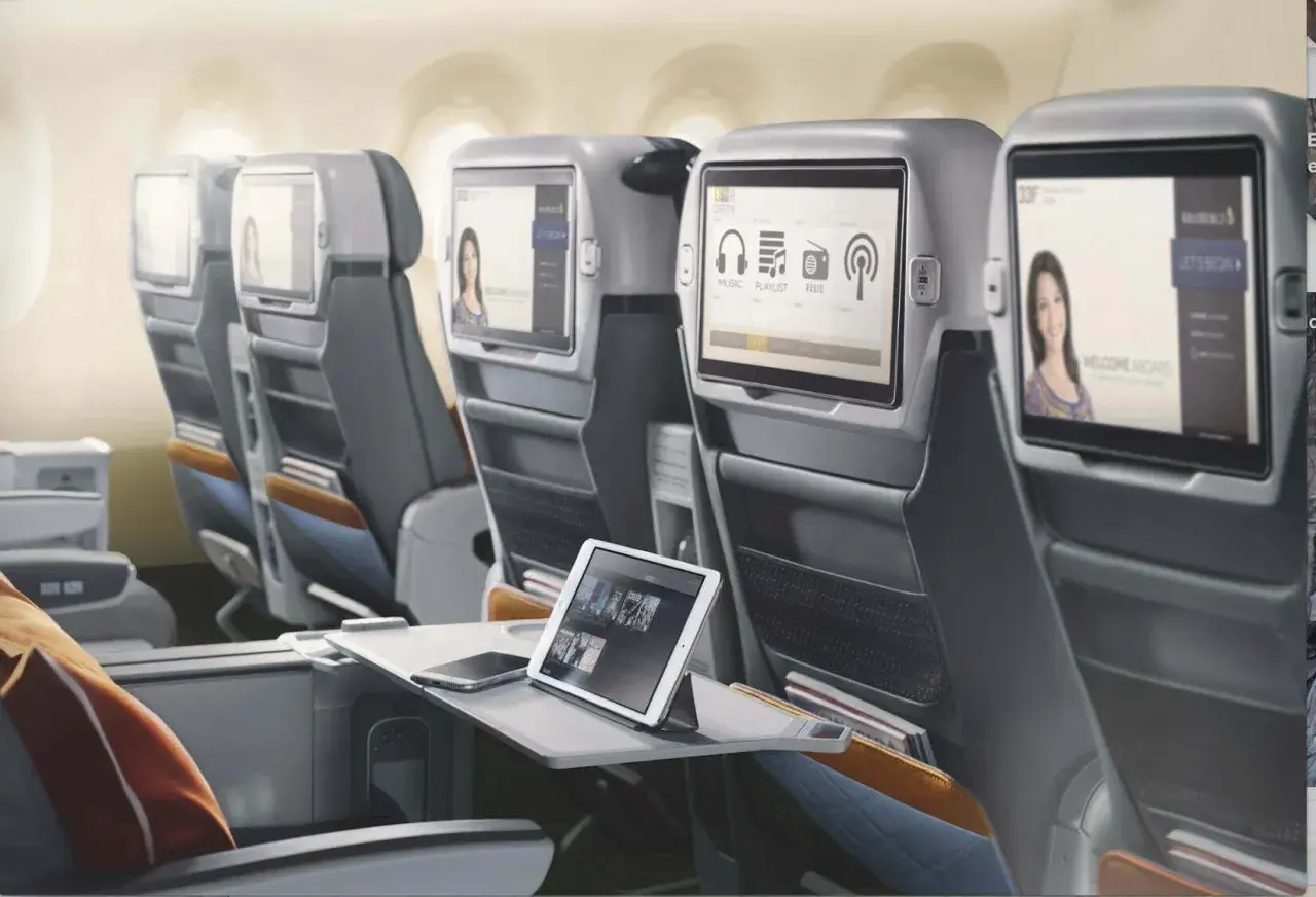 Komfortowe fotele w klasie lot premium economy. Ekrany rozrywki pokładowej, tablet i telefon na stoliku.