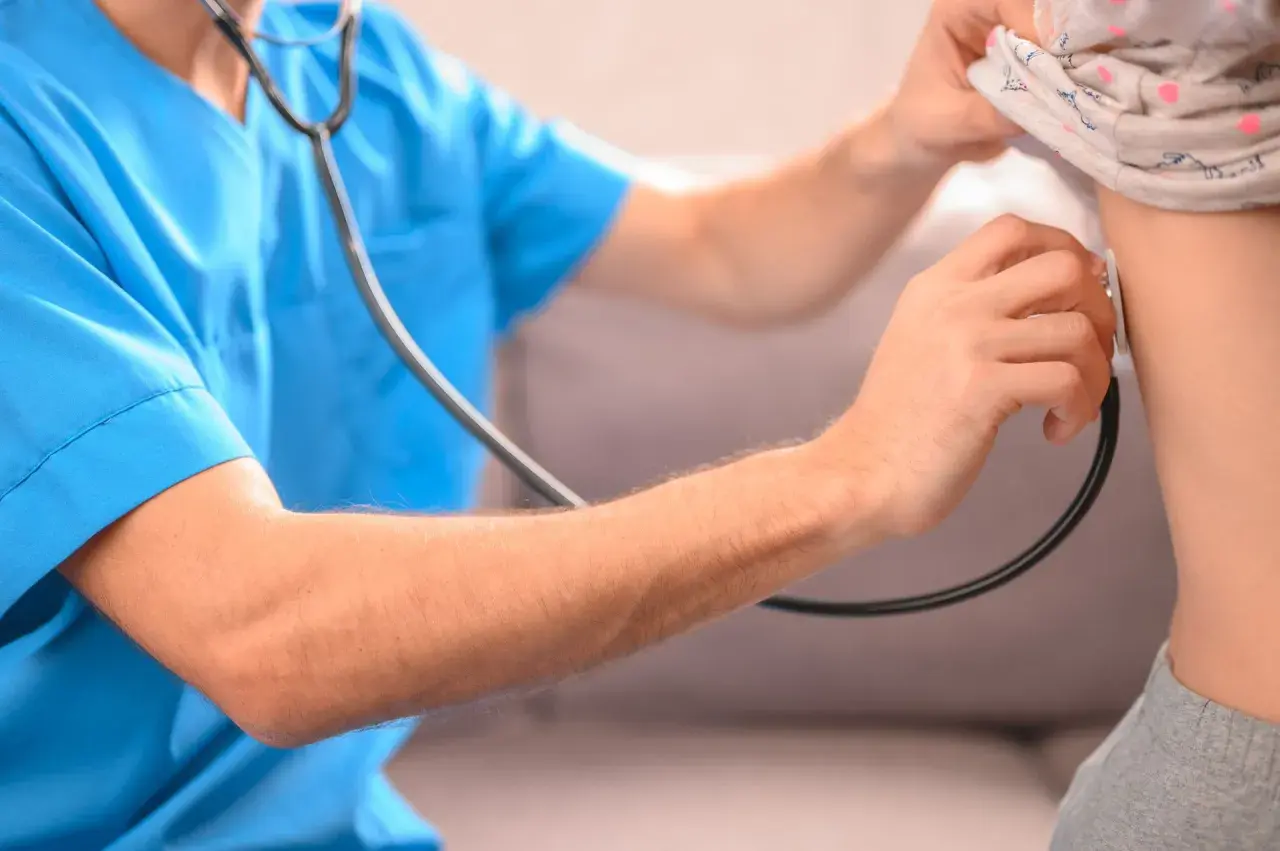 Lekarz osłuchuje klatkę piersiową dziecka, diagnozując zapalenie płuc.