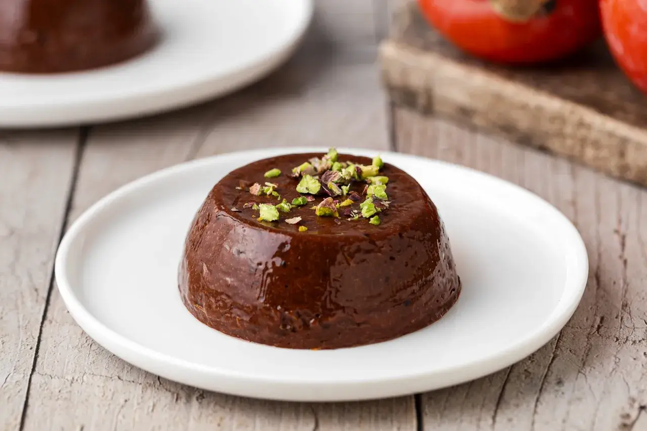 Budino di cachi al cioccolato, guarnito con pistacchi tritati, servito su un piatto bianco.