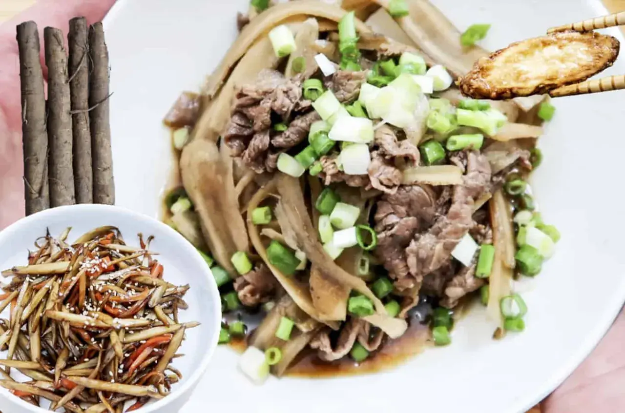 A delicious dish of braised burdock with thinly sliced beef and green onions, served on a white plate. A small bowl of burdock stir-fry is on the side.