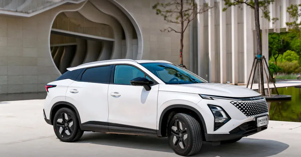 Biały OMODA hybryda zaparkowany przed nowoczesnym budynkiem. Stylowy SUV z charakterystycznym grillem i dynamiczną linią nadwozia.