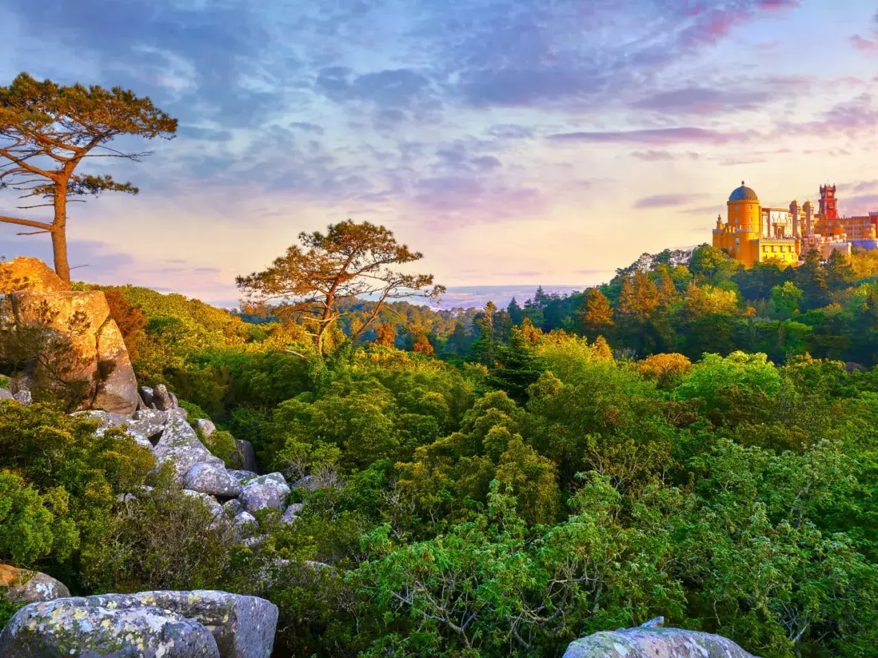 A vibrant Sintra hiking trail leads through lush greenery towards a colorful palace perched on a hill.