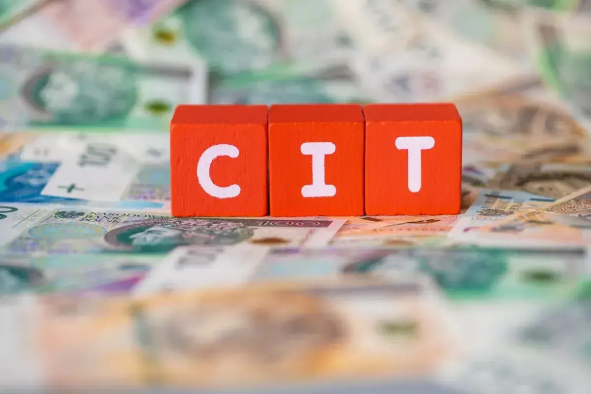 Trzy pomarańczowe klocki z literami "C", "I", "T" leżą na tle polskich banknotów. Podatek CIT to ważna część finansów.