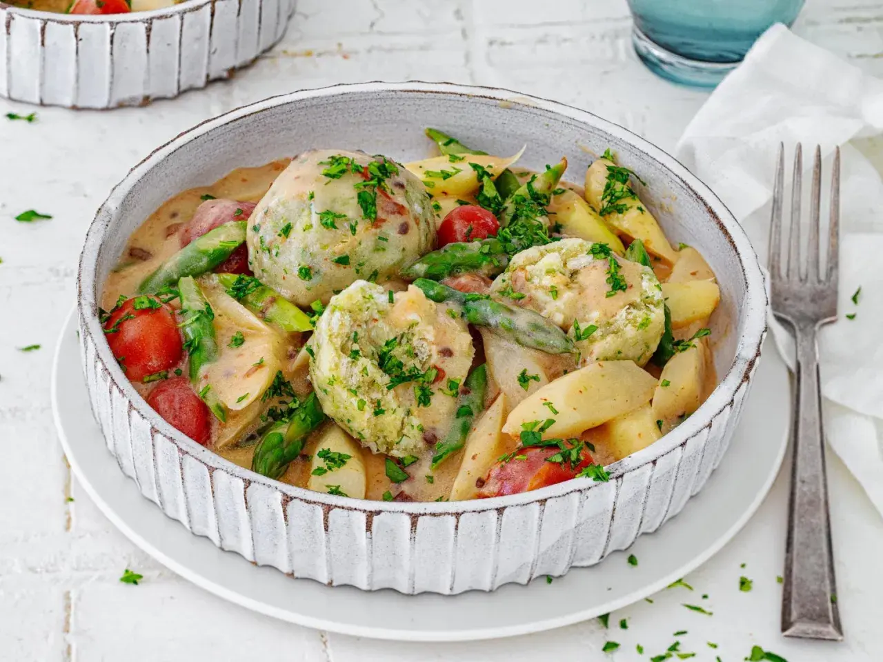 Spargel mal anders: cremiger Eintopf mit Klößen, Kartoffeln, Kirschtomaten und grünen Bohnen, garniert mit Petersilie.