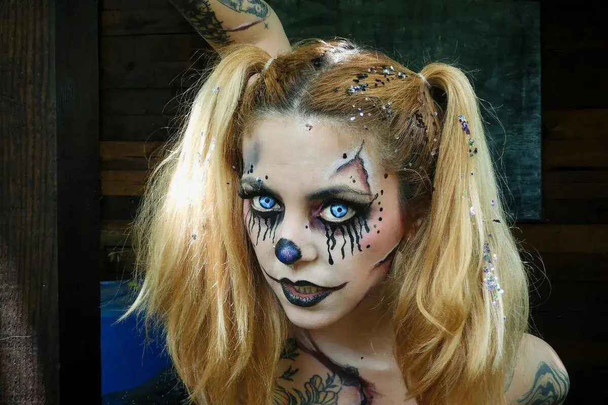 Chica con maquillaje de halloween de payaso aterrador, ojos azules brillantes, nariz de payaso y purpurina en el cabello.