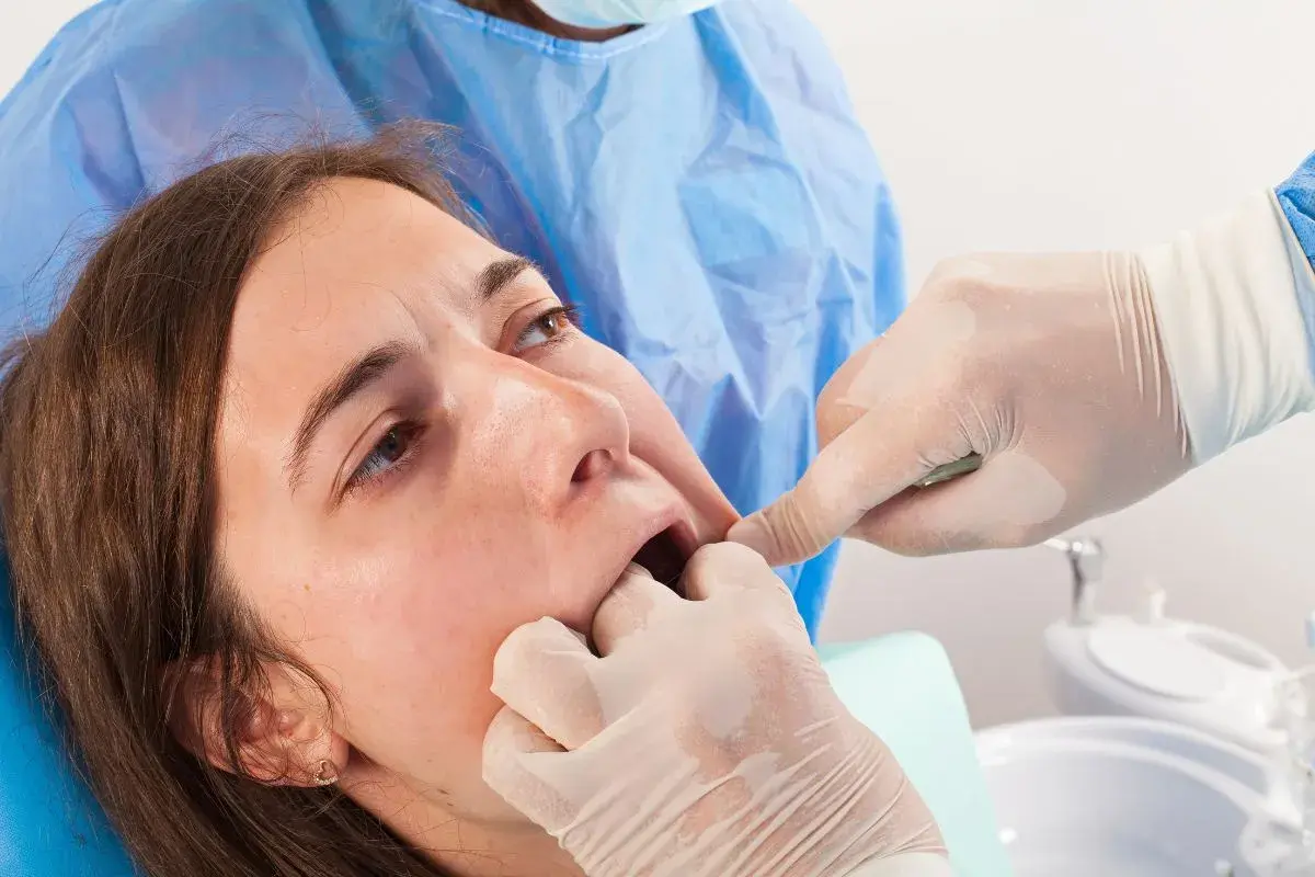 Dentista examina la boca de una paciente, notando un posible coagulo muela blanco.