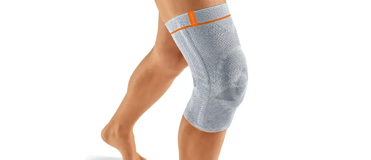 Ein Bein mit einer grauen Kniebandage. Die Bandage könnte bei falscher Anwendung oder zu engem Sitz Schmerzen verursachen.