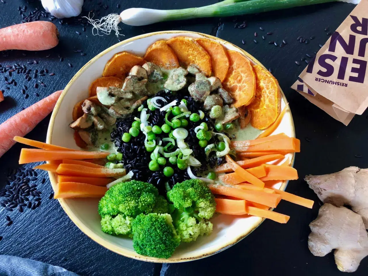Bunter Reisschüssel mit schwarzem Reis, Süßkartoffeln, Brokkoli, Karotten, Erbsen und Pilzen in cremiger Sauce. Ein Gericht, das reich an Kohlenhydraten ist.