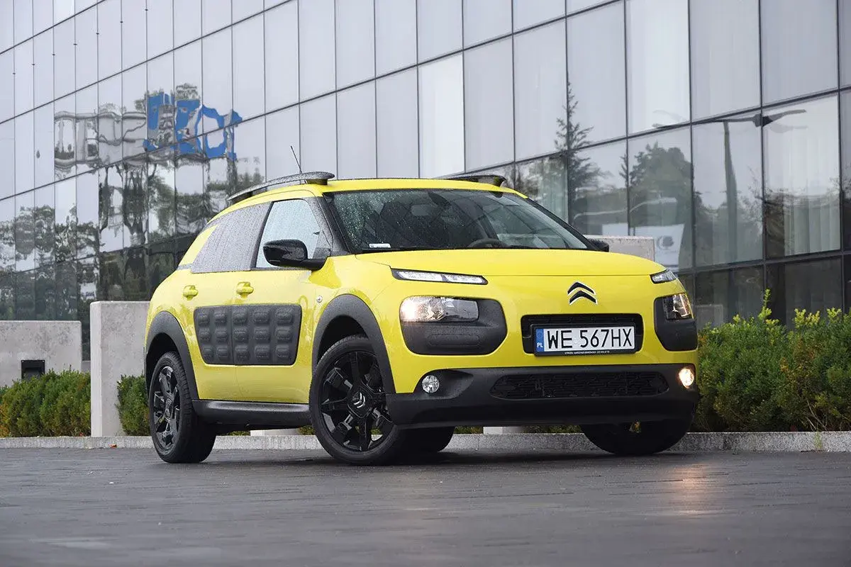 Żółty Citroen C3 Cactus z czarnymi felgami i charakterystycznymi panelami Airbump stoi przed nowoczesnym budynkiem.