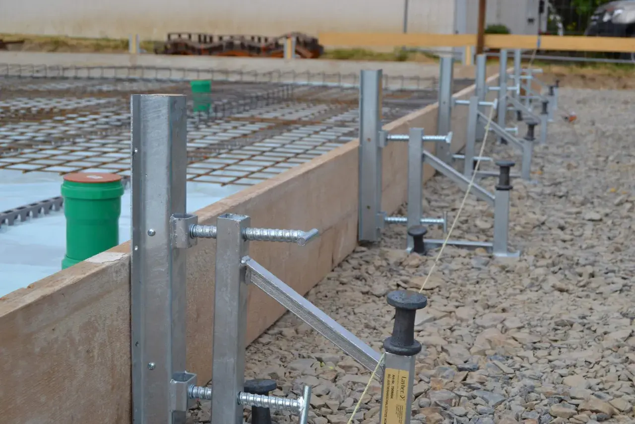 Stahlstützen und Holzbretter bilden die schalung wand für eine Betonplatte. Bewehrungsstahl und grüne Rohre sind sichtbar.