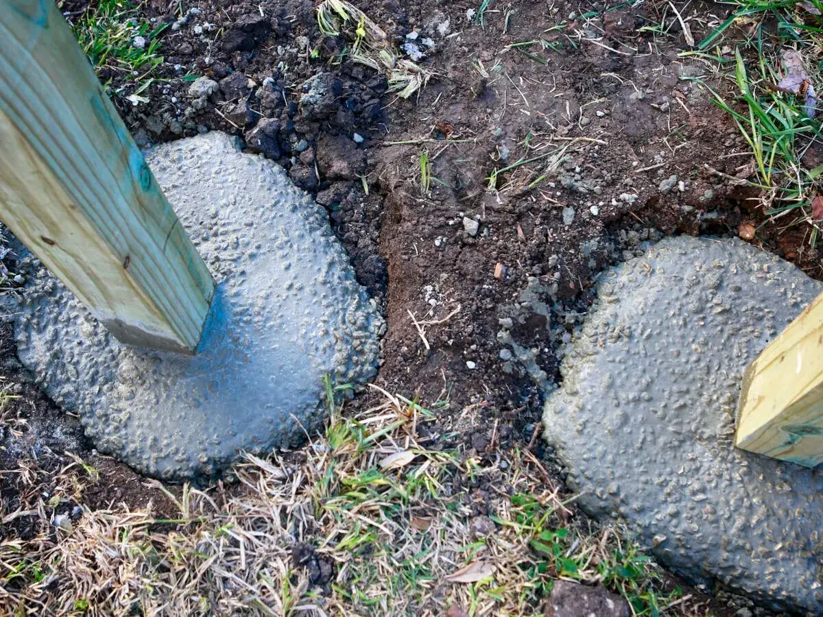 Holzpfosten werden in frischen Beton gesetzt. Die Tiefe, wie tief man einen Pfosten einbetonieren sollte, hängt von der Nutzung ab.