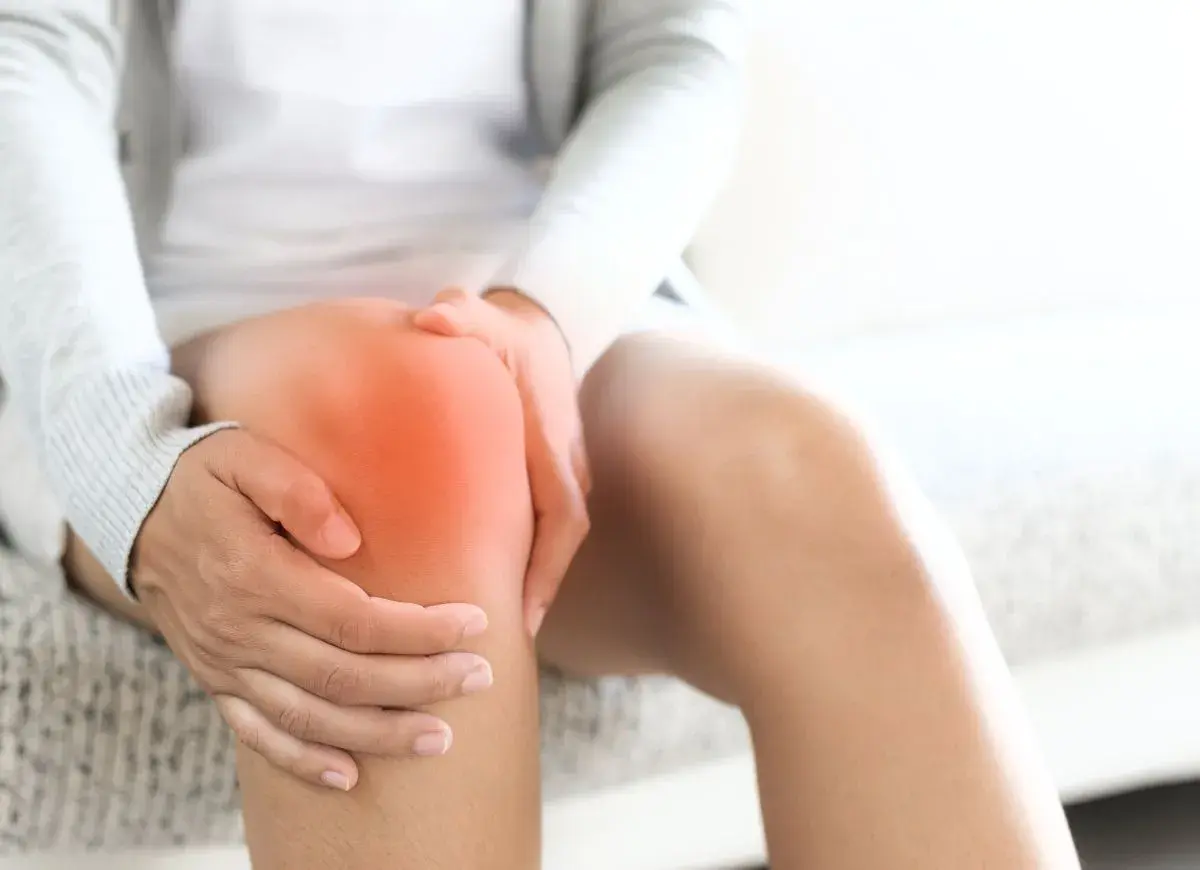 Person hält schmerzendes Knie, das rot leuchtet. Richtige Schuhe können bei Knieschmerzen helfen.