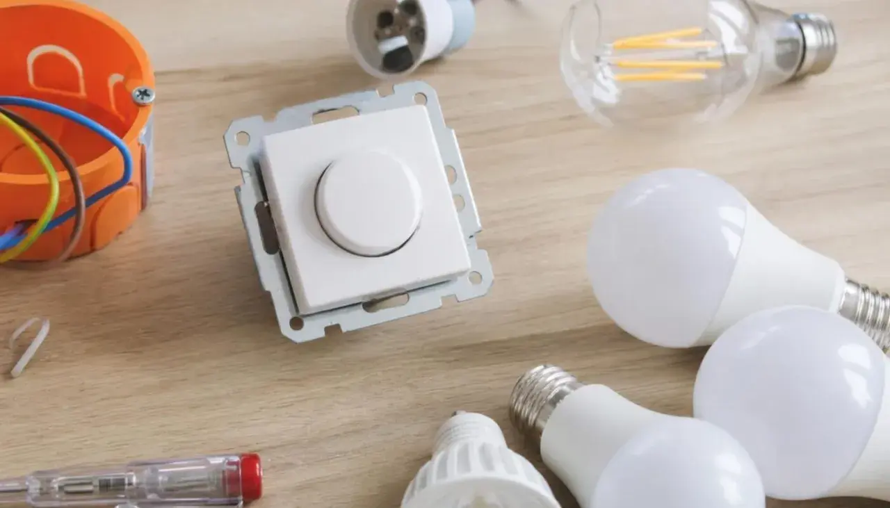 Ściemnianie led: biały ściemniacz, żarówki led, puszka instalacyjna i śrubokręt na drewnianym blacie.