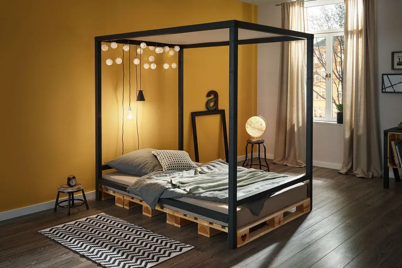 Ein modernes Himmelbett, das man leicht selber bauen kann, mit Paletten als Basis. Lichterketten und eine gelbe Wand schaffen Gemütlichkeit.
