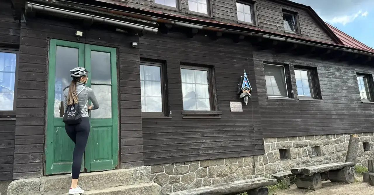 Kobieta w kasku rowerowym zbliża się do drzwi schroniska Chatka Górzystów.