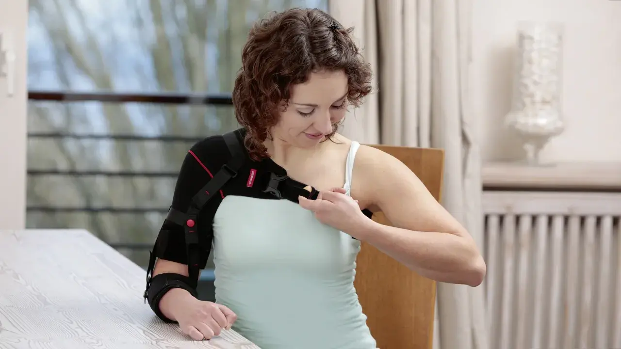 Frau legt sich eine Armorthese an, um ihre Schulter zu stabilisieren.