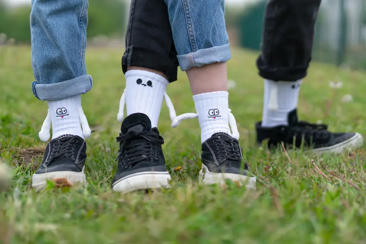 Jak nosić długie skarpety? Zabawne białe skarpety z postaciami i czarne trampki na trawie.