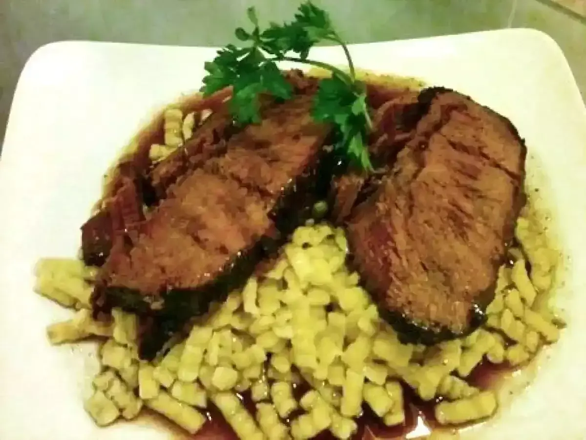 Tranches de brasato al barolo, tendres et savoureuses, servies sur un lit de pâtes fraîches, garnies de persil.