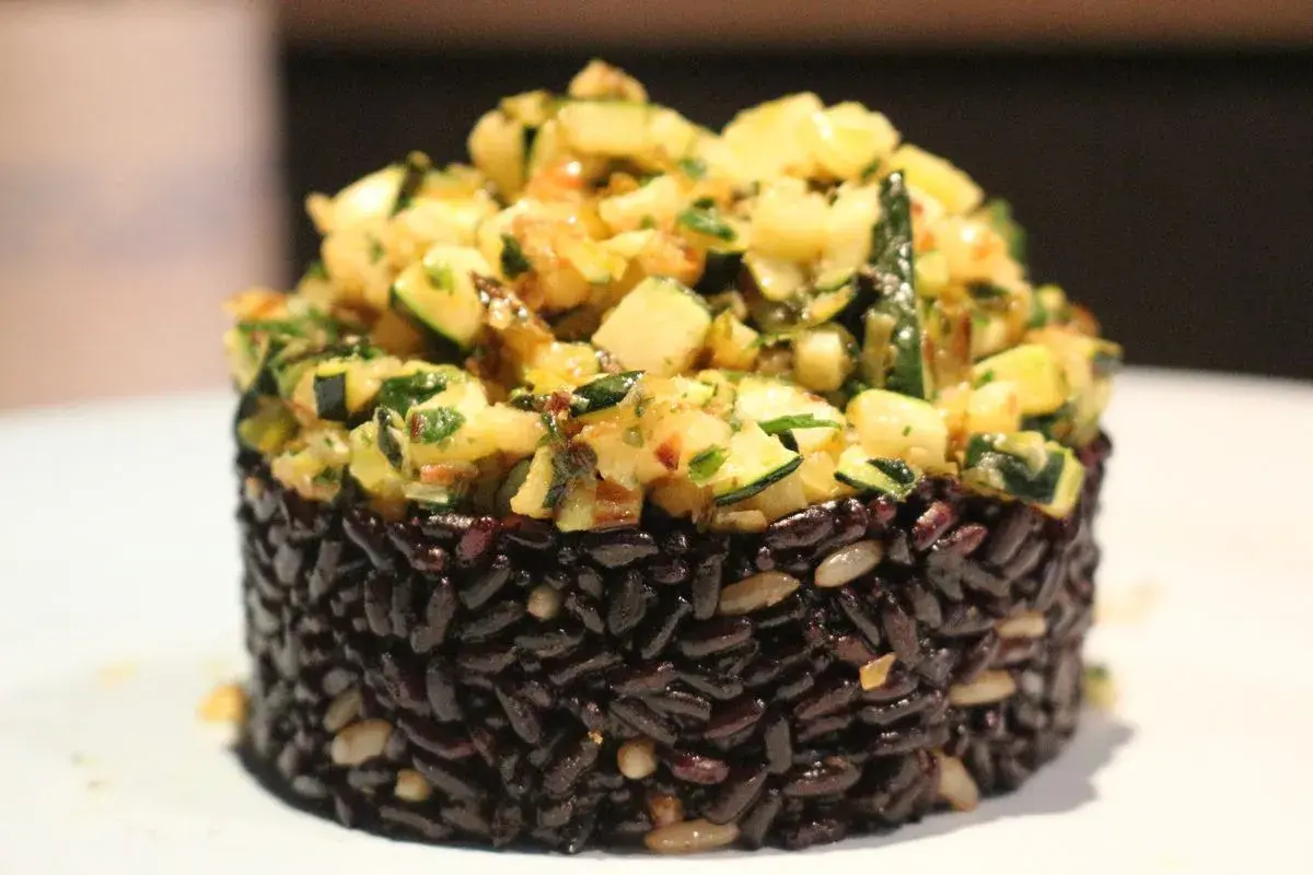Riso nero compattato a cilindro, guarnito con un'abbondante porzione di zucchine saltate e erbe aromatiche.