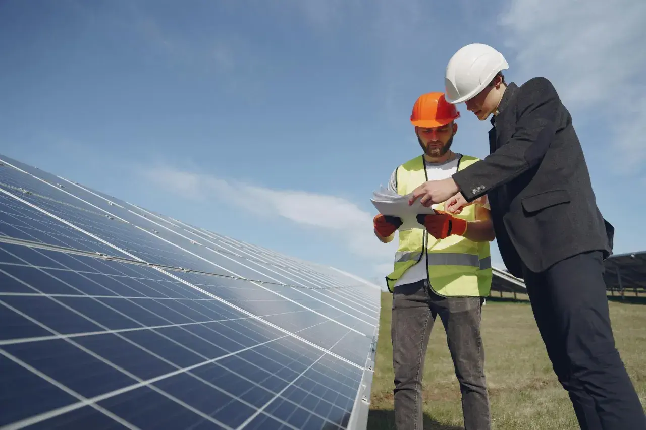 Deux hommes en casque discutent des plans près de panneaux solaires, en vue du remplacement d'un appareil sous garantie.