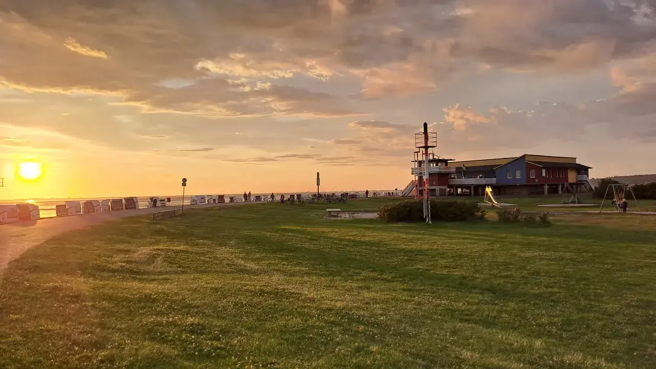 Sonnenuntergang am Husum Strand mit Strandkörben, einem Spielplatz und einem bunten Gebäude.