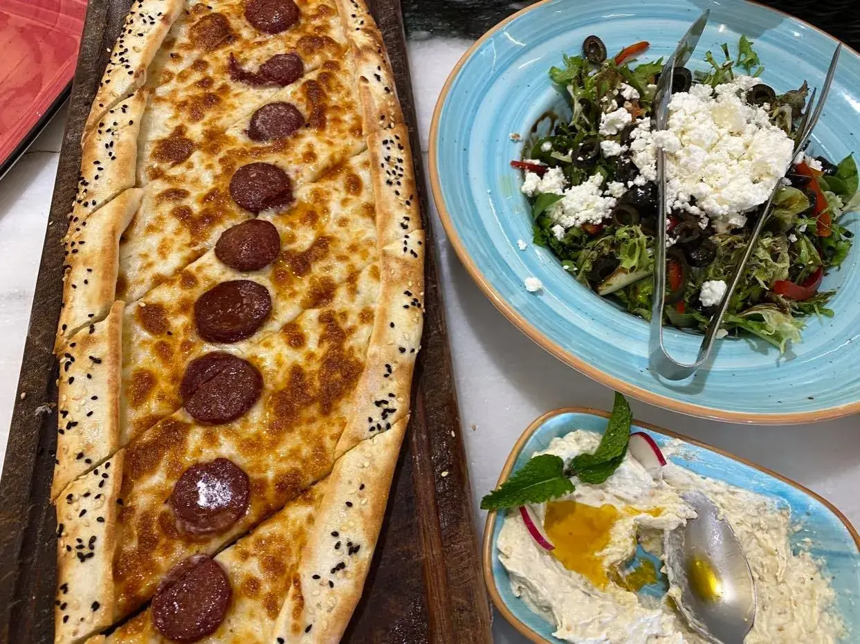 Pyszna pide z kiełbasą i serem, sałatka z fetą i oliwkami, oraz pasta z cieciorki. Smaczne jedzenie, które może być częścią wrażeń z cen w Dubaju.