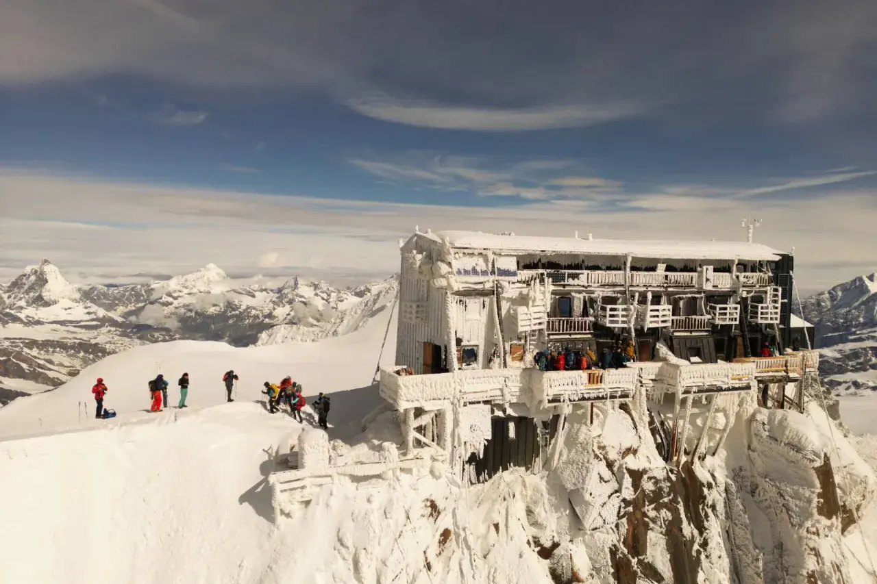 Die Capanna Margherita thront eisbedeckt auf einem Berggipfel. Bergsteiger genießen die Aussicht auf die verschneite Alpenlandschaft.