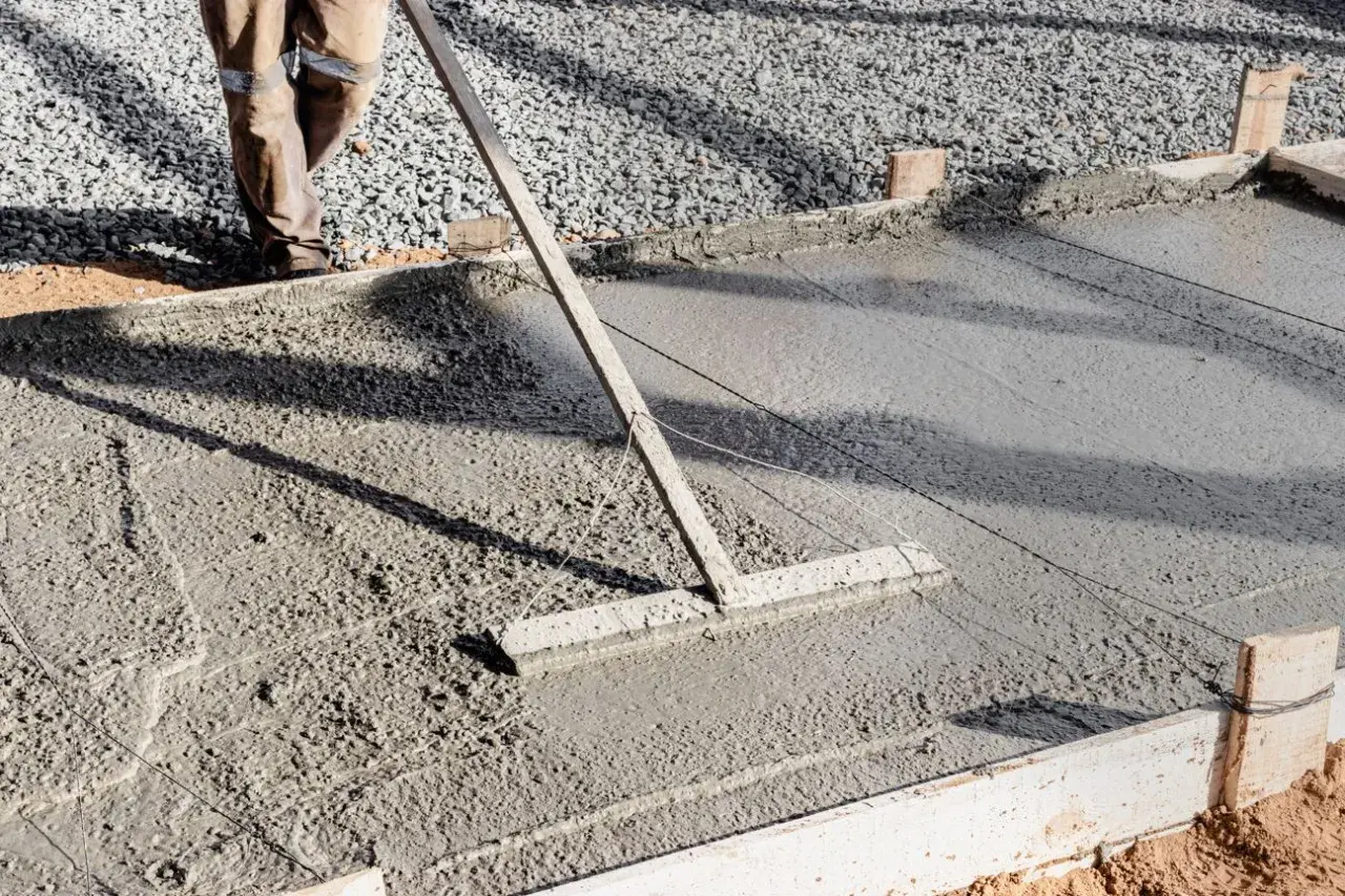 Un ouvrier lisse une **pente en béton** fraîchement coulée avec un râteau, créant une surface lisse pour une nouvelle construction.