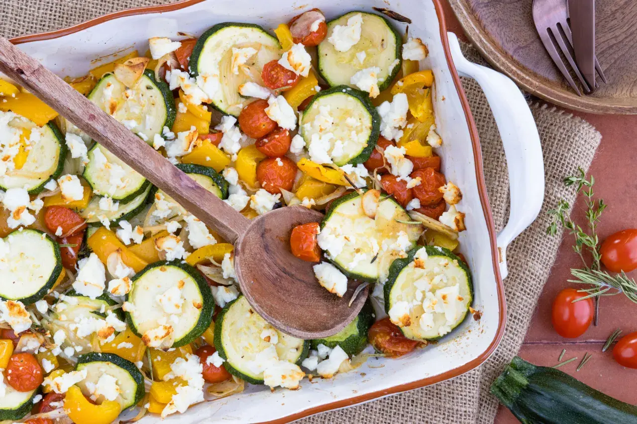 Gebackener Feta mit Zucchini, Kirschtomaten und gelber Paprika in einer Auflaufform, bereit zum Servieren.